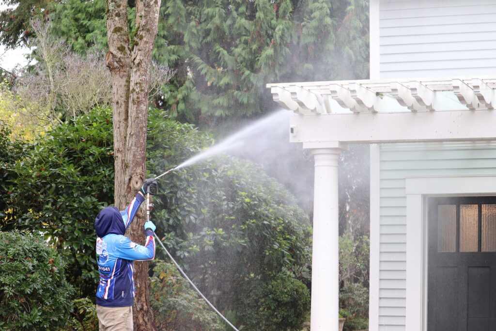 Homefront Power Wash Employee washing a white wooden trellis on a house in Medina, WA